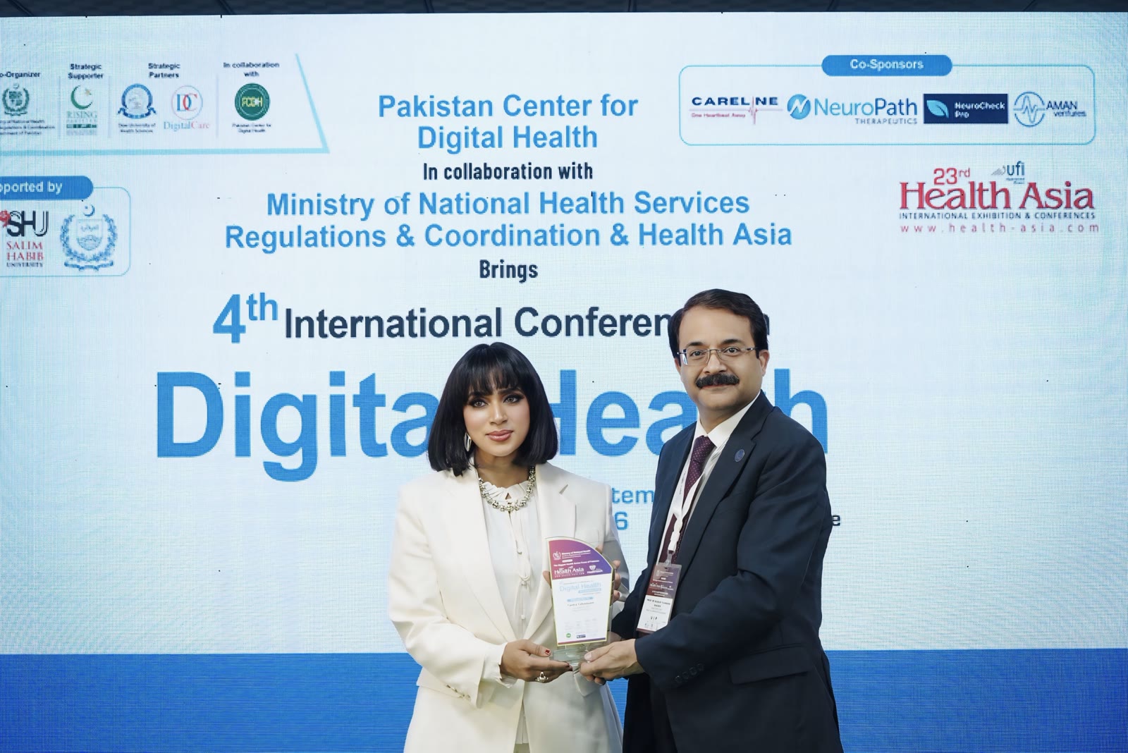 Tanha Tabassum on stage with a conference official in front of the Digital Health conference screen